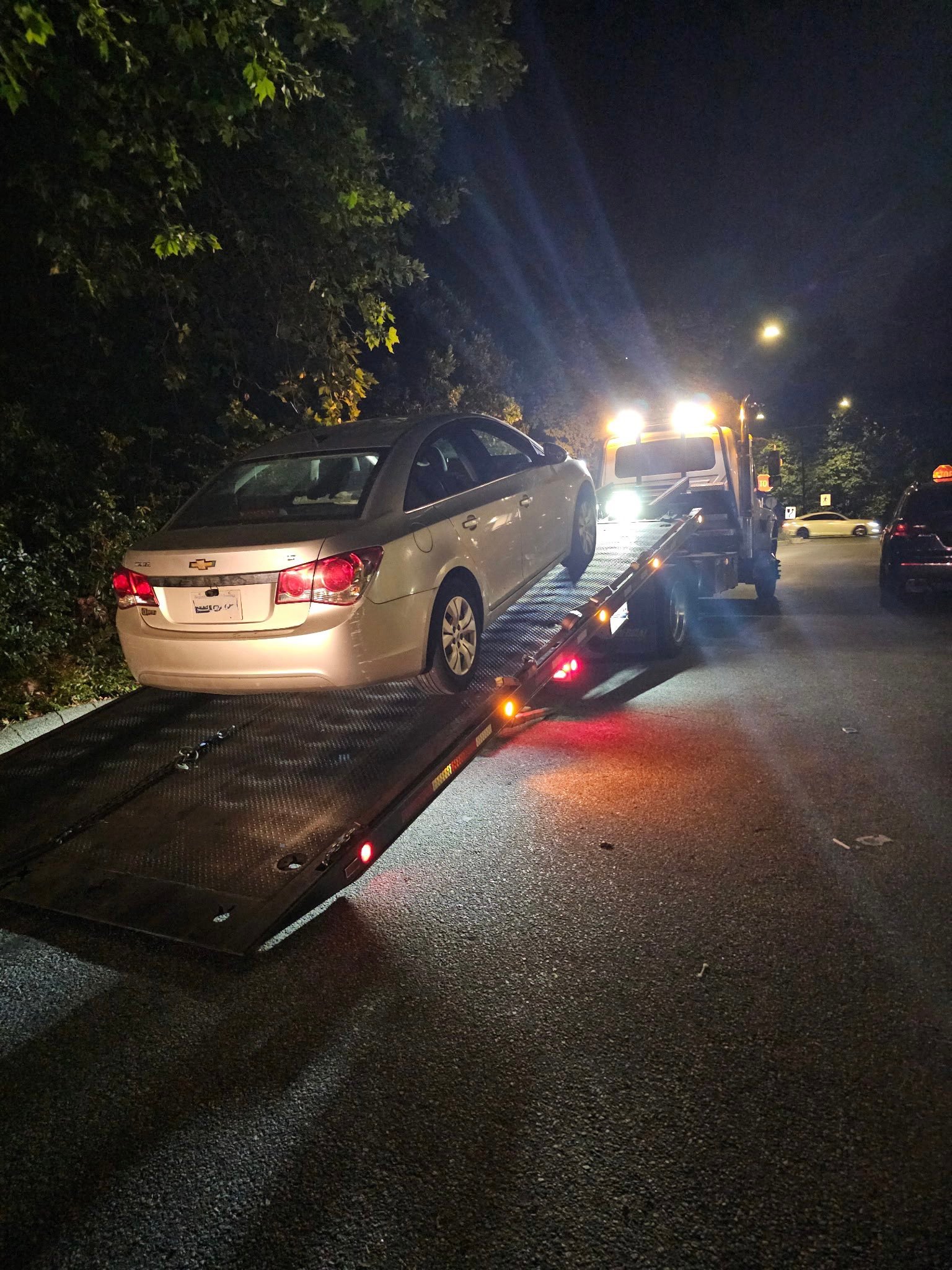 White car loaded onto a tow truck at night