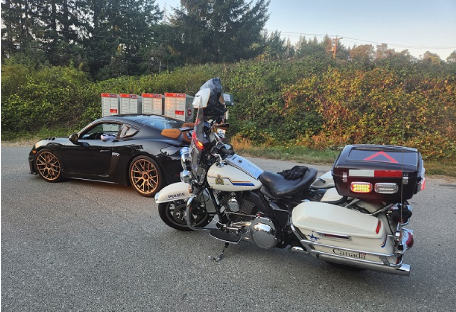 BC Highway Patrol motorcycle stopped behind a black Porsche 718 GT4 RS after the car was impounded for excessive speeding on the Island Highway